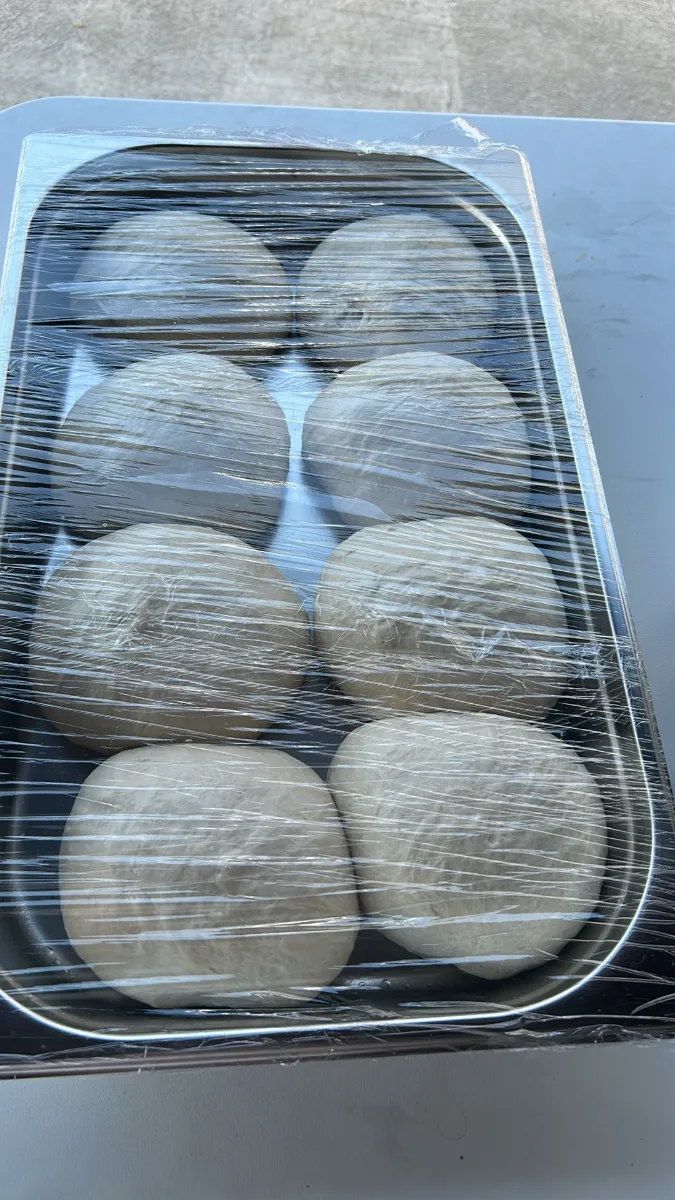 Nyolc pizzatésztagombóc fóliával letakart tálcán