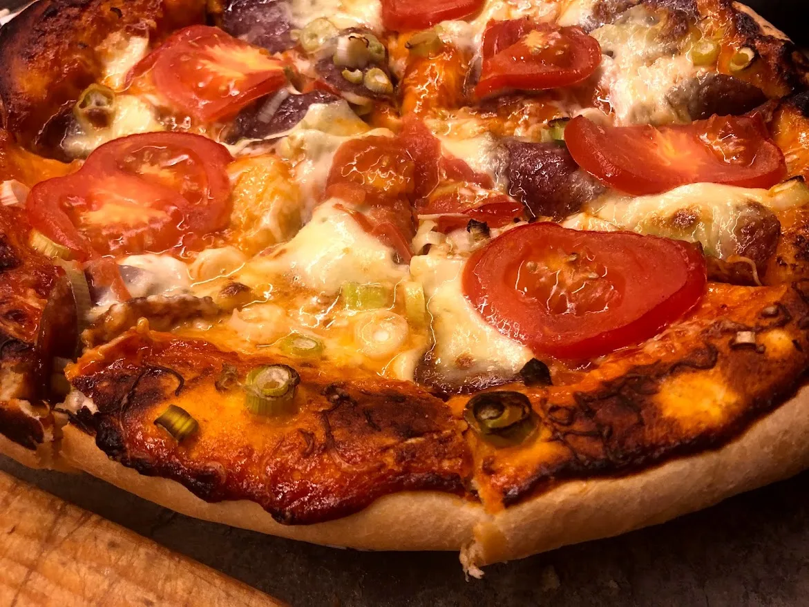 Házi pizza pirult peremmel, olvadt sajttal, paradicsommal és szalámival