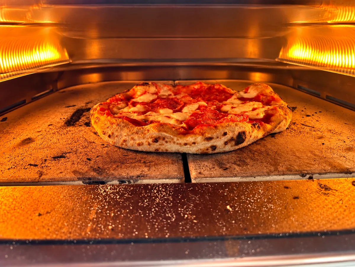 Piruló pizza a pizzasütő kőlapján, izzó fűtőszálak alatt